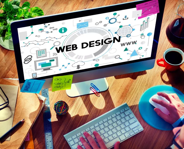 A desktop monitor showing the words Web Design surrounded by interface icons, with a person typing at the keyboard.